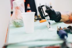 Hands in latex gloves filling dark tattoo inks in pots