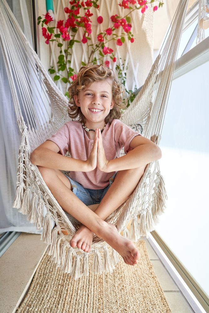 Smiling kid sitting on hammock chair and gesturing namaste