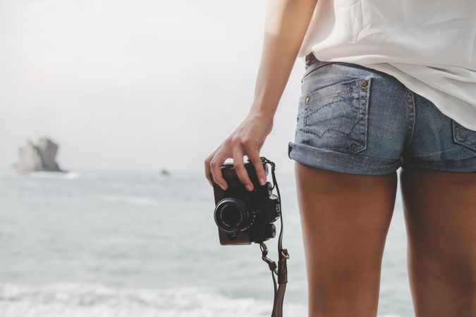Woman with camera on shore near stones and water