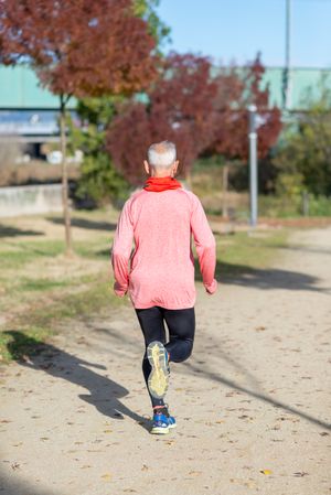 Back of mature man in red shirt jogging outside in park