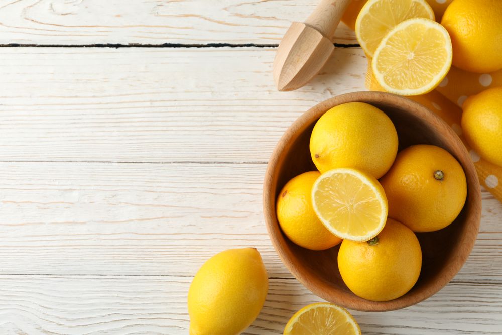 Bowl, lemons and wood juicer on wooden background, top view