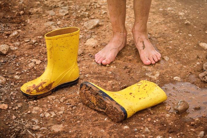 Barefoot kid standing on ground near gumboots