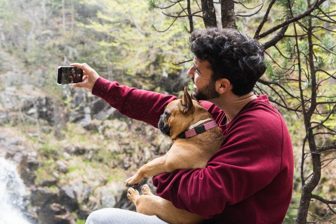 Smiling traveling man taking selfie with dog in forest