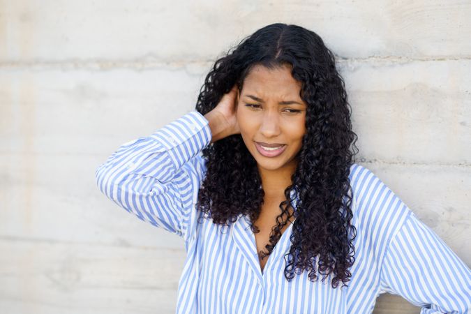 A Young Woman with Curly Hair, Dressed in a Striped Shirt, Stands Against a Concrete Wall