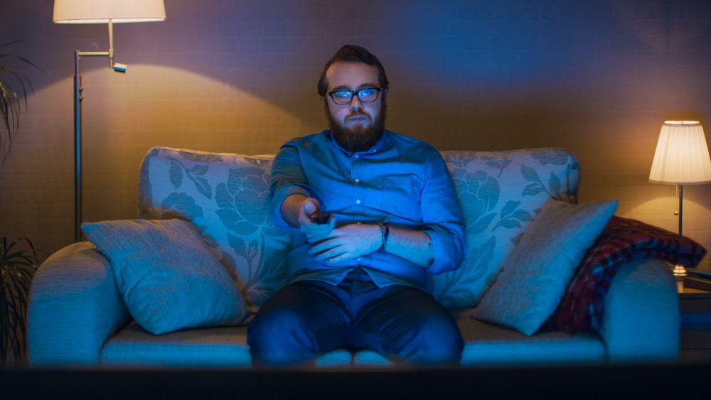 Portrait Shot of a Man Sitting on a Sofa in His Living Room, Watching TV, Changing Channels.