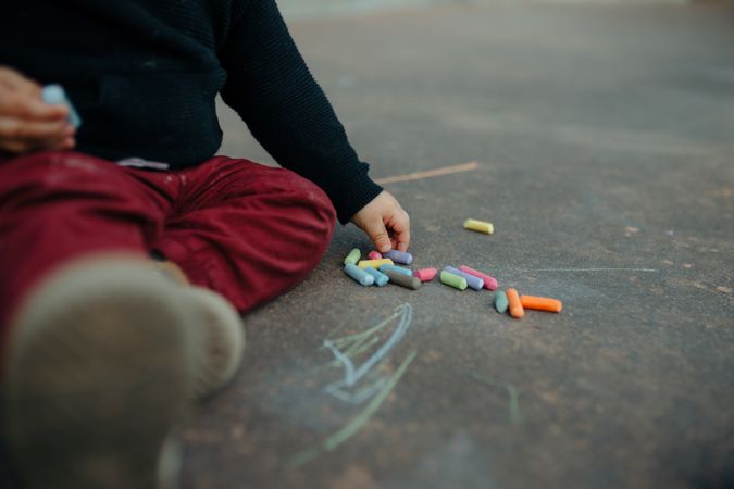 Child sitting on ground with chalk sticks