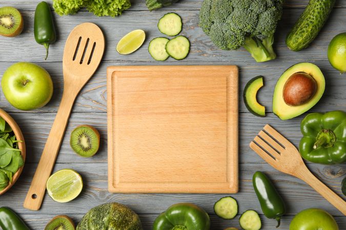 Board, fork, spoon, vegetables and fruits on wooden table