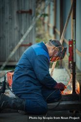 Man in blue uniform and goggled welding a rod outdoor 0KQnA4