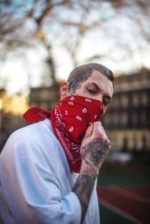 Young tough guy in red bandana with face tattoos furrowing brow at camera outside