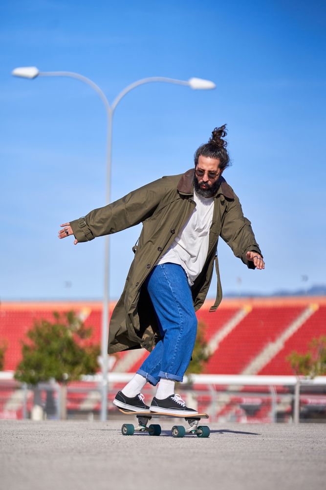 Stylish hipster in trench coat and jeans riding skateboard