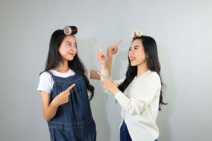 Two Asian Female Friend Smiling Pointing at Each Other Hair Roller