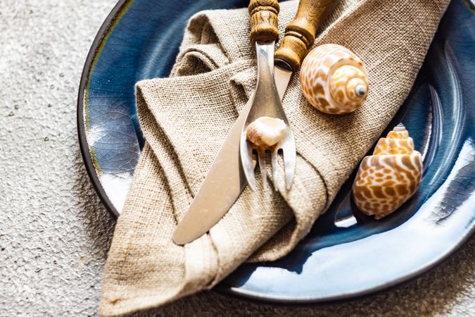 Marine cutlery set with shells on grey concrete background with copy space