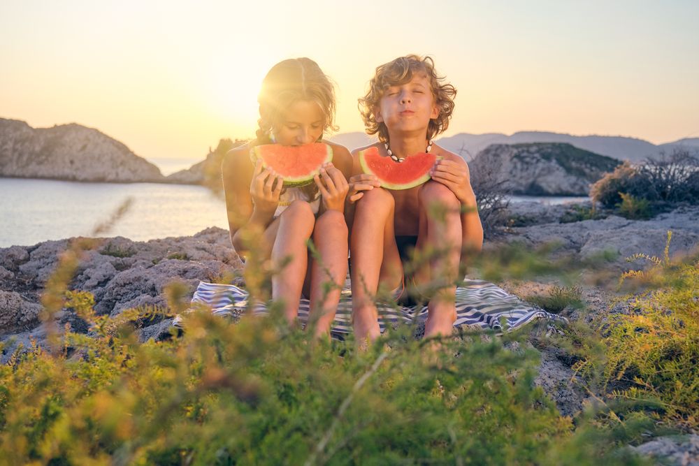 Happy siblings eating watermelon on seashore