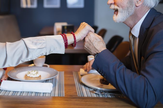 Grey bearded man taking woman’s hand over restaurant table