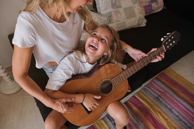 Girl looking and smiling at a woman who's teaching her to play guitar