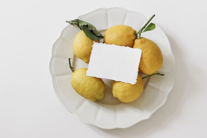 Fresh yellow lemons, dry green leaves on plate with mock up card