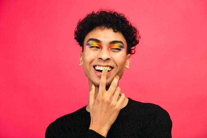 Happy young man wearing rainbow colored eye shadow and smile face nail paint