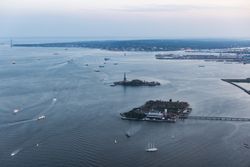 Aerial Helicopter Cinematic Passing View of the Statue of Liberty with Manhattan Skyline Cityscape. Panoramic View of New York City Skyscrapers and Jersey City Buildings on a Cloudy Afternoon