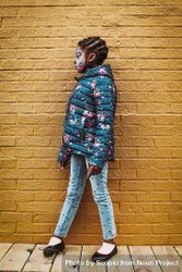 Side view of Black girl with face paint standing beside yellow brick wall 5aMOQ5