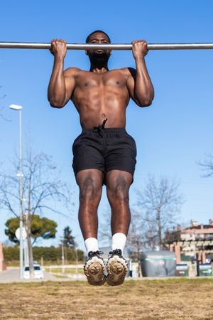 Strong Black sportsman working out on bar in town