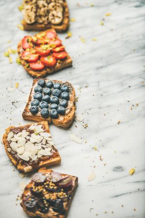 Toast topped with fresh fruit on marble background, vertical composition with copy space