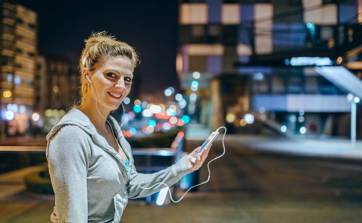 Portrait of smiling blonde sportswoman listening music on mobile phone application
