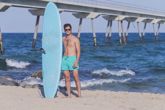 Full body shot of male surfer standing in the rocks on the coast near pier