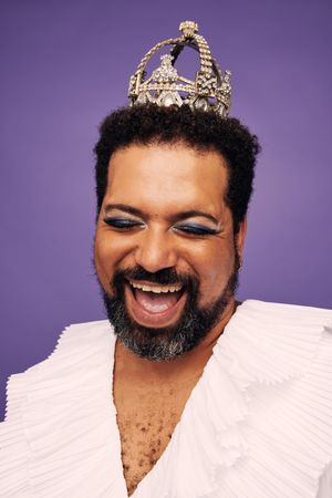 Bearded man wearing crown and makeup laughing