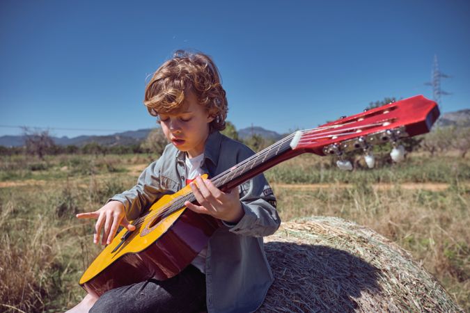 Cute kid playing guitar on hay bale in field