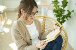 Cropped shot of A woman reading a book sitting in a chair with a comfortable posture.