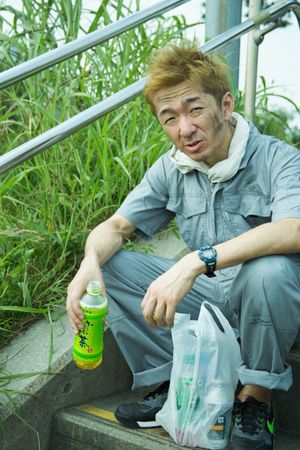 Exhausted worker in work suit sitting on staircase holding a green bottle
