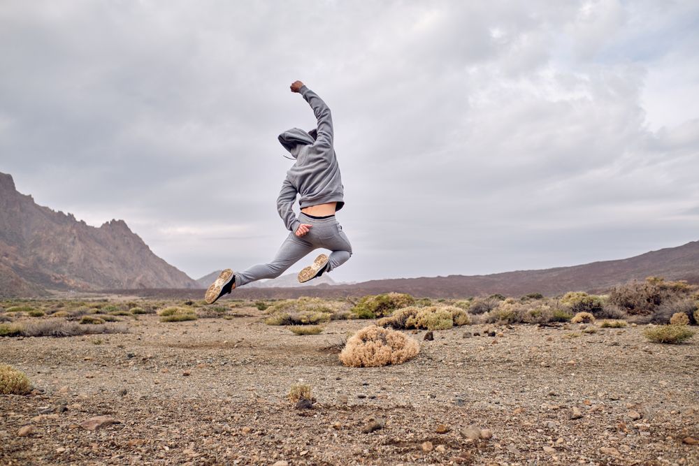 Carefree man traveler jumping on rocky ground near hills