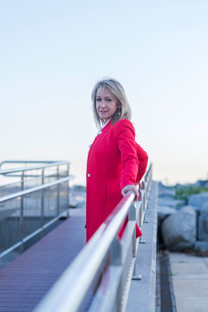 Side of woman in red coat leaning on railing of pedestrian bridge