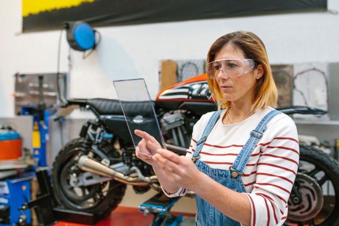 Female mechanic with security glasses touching transparent tablet
