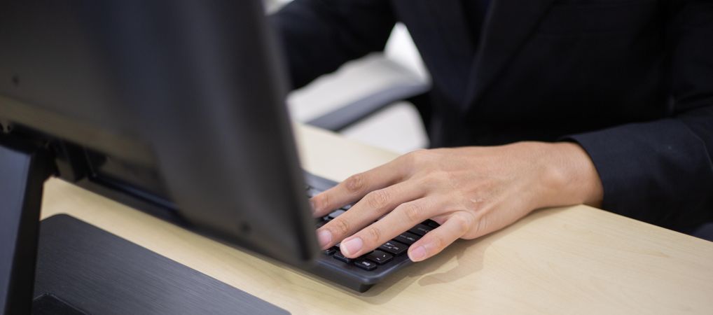 Hand of male employee typing on computer keyboard at desk