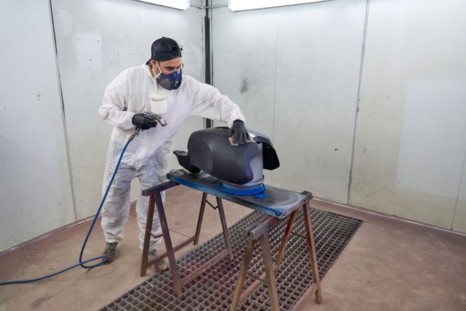 Male mechanic painting motorbike tank in garage