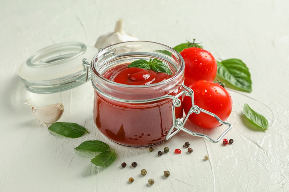 Composition with fresh tomatoes, basil, pepper, garlic and sauce in glass jar on studio background, space for text