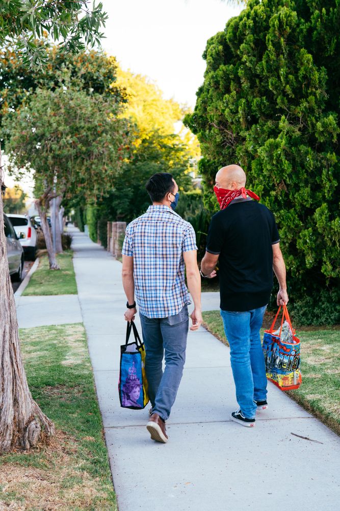 Full length back view of a couple wearing masks and talking while carrying grocery bags outside