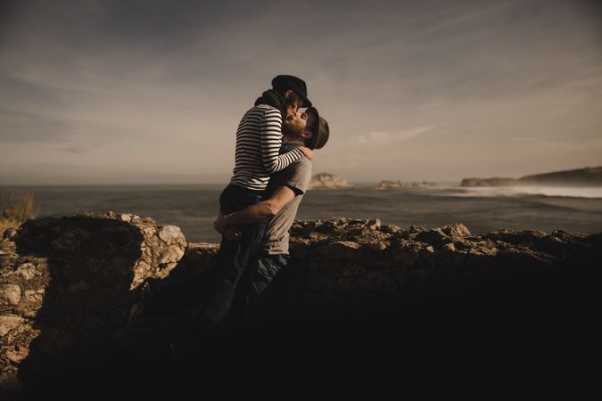 Man kissing and holding woman on hands near stones on shore
