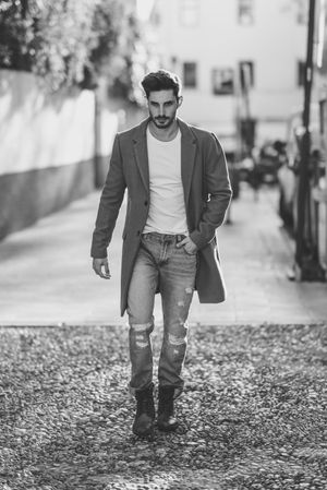 Man in smart winter jacket and jeans walking on street, b&w