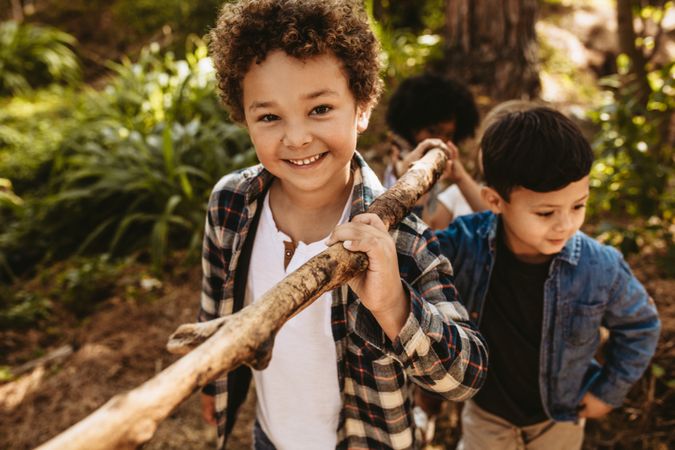Cute boy carrying a stick with friends in forest