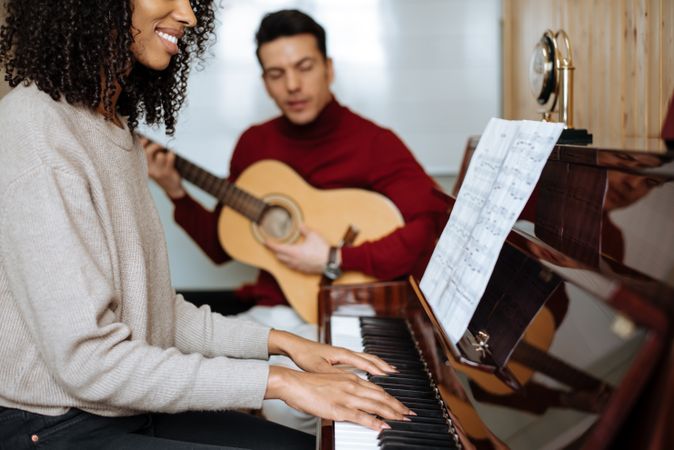 Woman playing piano near man playing guitar in studio