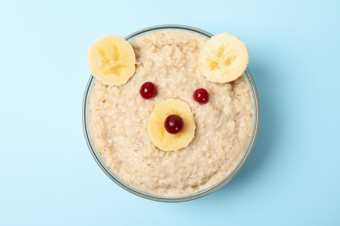 Bear face made of porridge and fruits on blue background, top view. Baby food