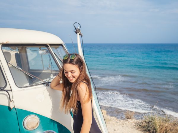 Woman smiling leaning on car on beach