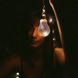Thoughtful woman with burning lightbulb in darkness