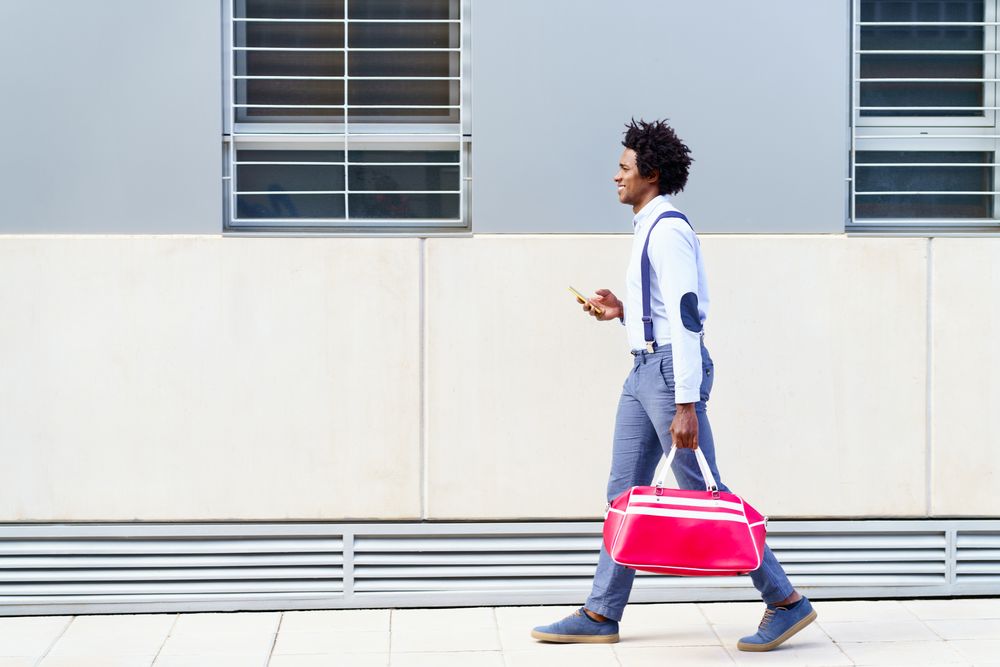 Side view of Black man with curly hair wearing shirt and suspenders walking on street