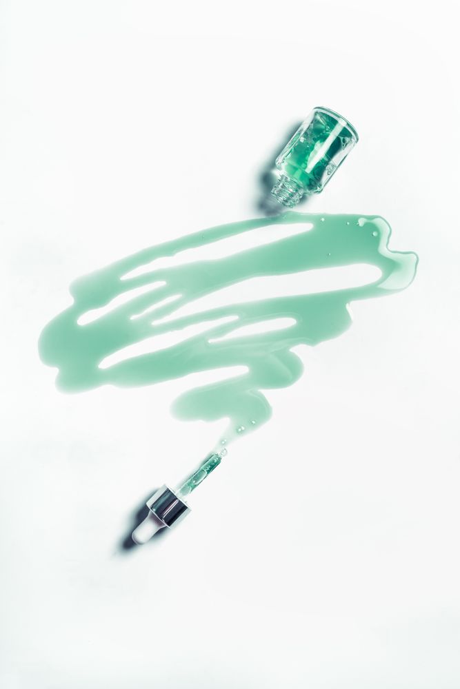 Blue cosmetic liquid leaking from glass pipette bottle. Moisturizing beauty product for facial treatment. Top view.