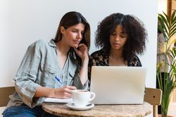 Multiracial girlfriends sharing laptop in coffee shop