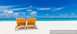 Two lounge chairs on an empty tropical beach with light sand 56JNL5