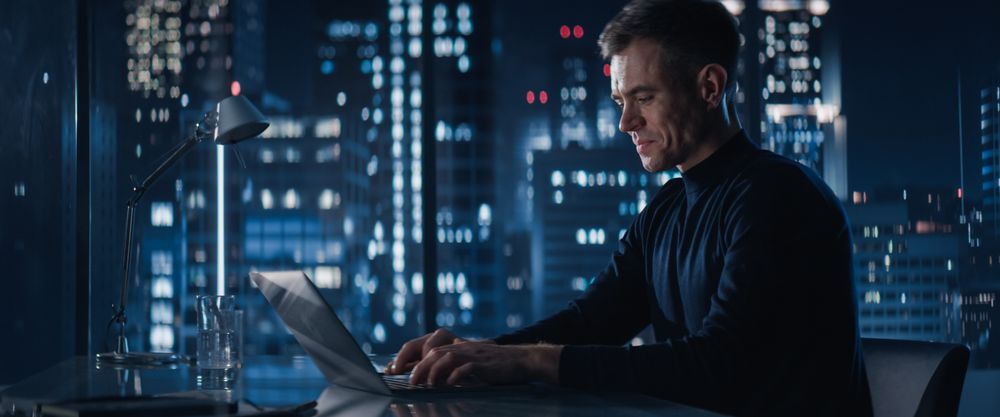 Close Up Portrait of Businessman in a Suit Standing Next to Window in Big City Office with Skyscrapers Late At Night.